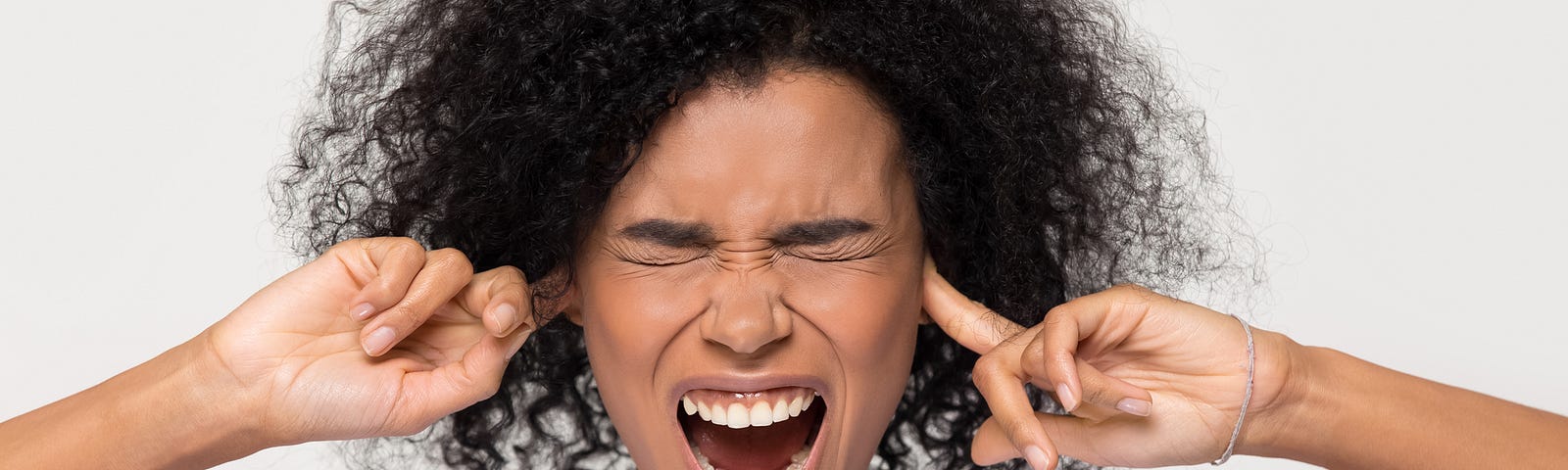 Woman with curly hair with fingers to her ears, eye closed and mouth open exclaiming