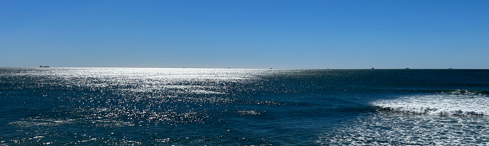 Queensland beach, brilliant blue sky, sun reflecting off the left side of the image, waves breaking on the right.