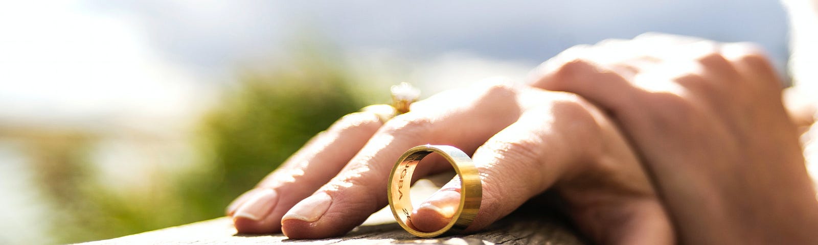 A hand resting on a wall. The tip of one finger is inside a wedding ring.