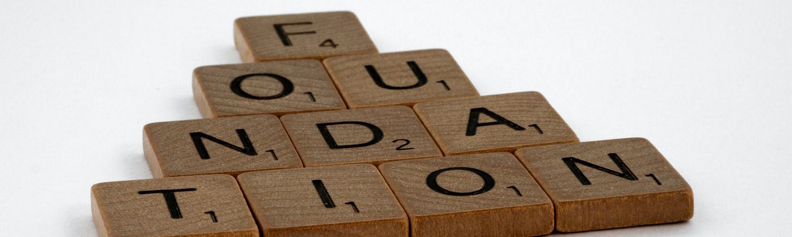 Wooden Scrabble tiles arranged like a flat pyramid. The letters spell “foundation”.