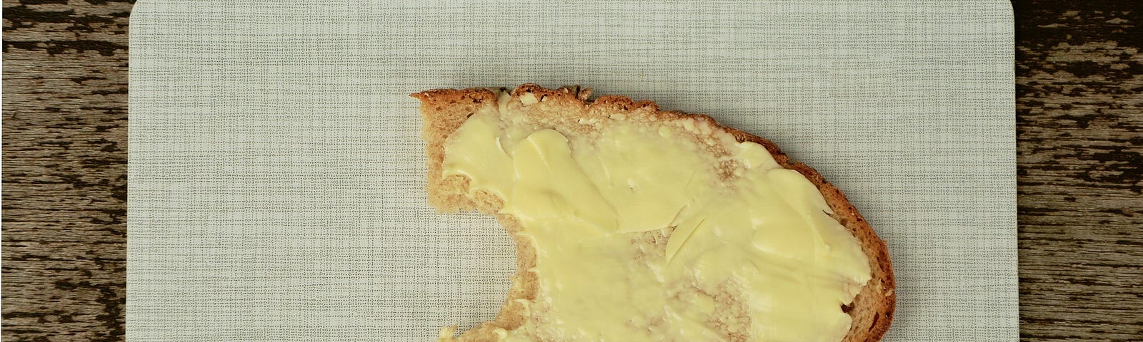 Slice of buttered bread on board. The bread has been nibbled on.