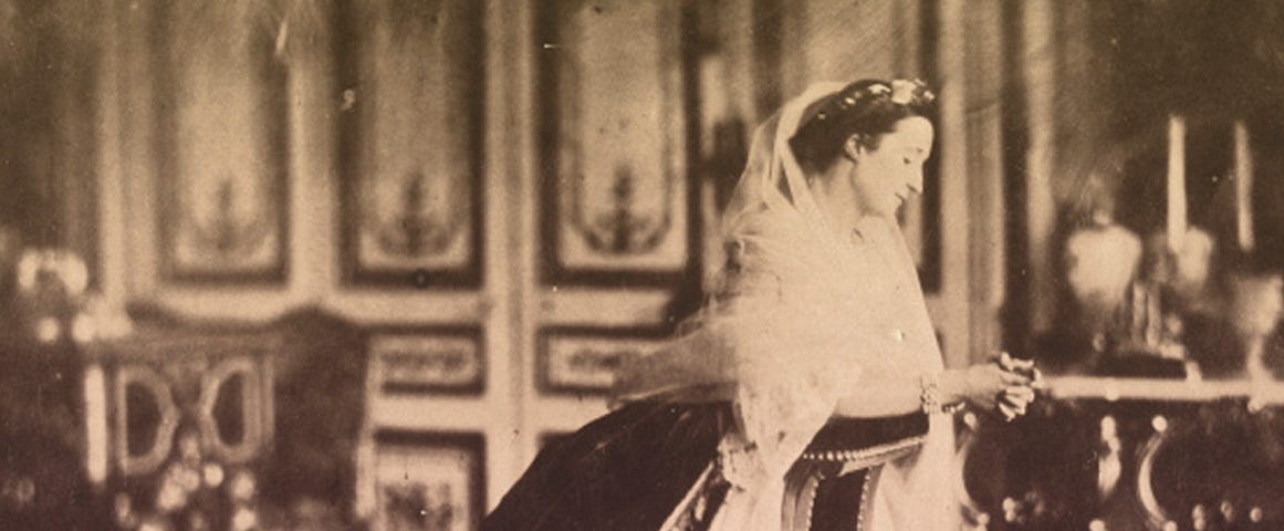 Empress Eugenie in her palace of St. Cloud, wearing a crinoline gown and a white veil.