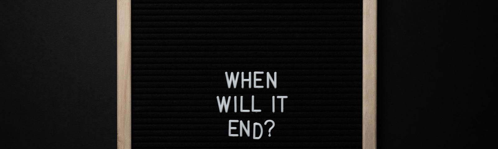 A wooden photo frame on black background. Inside, white letters spell the words “when will it end?”, underneath each other. The end tapers off as if falling from the frame.