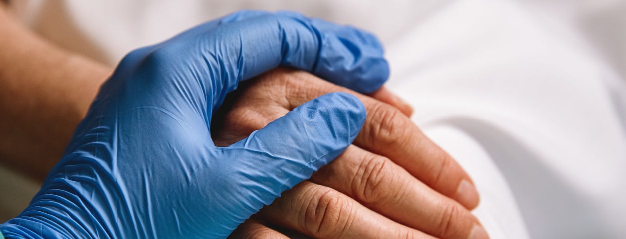 Close up of a doctor hand with blue glove giving support and love to a patient at hospital. Coronavirus pandemic concept.