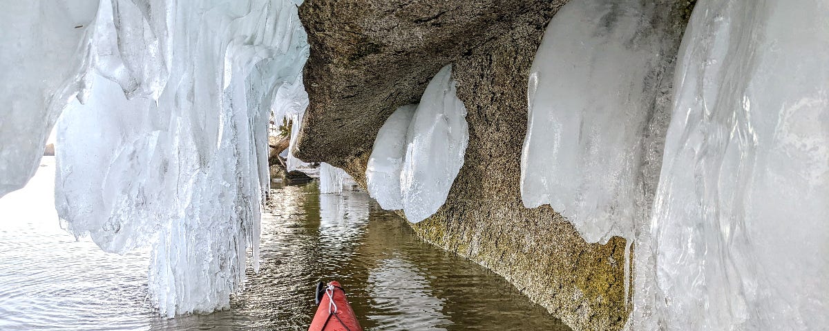 The bow of a red kayak at the entry of an ice cave.