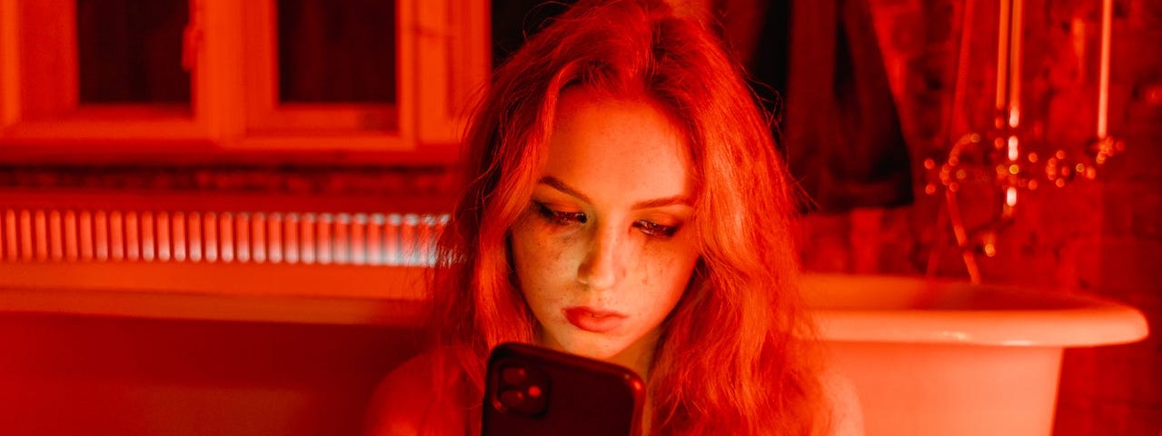 A woman cries while sitting beside a bathtub and looking at her phone