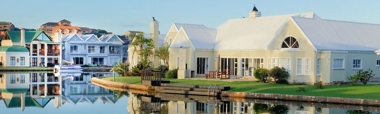 A neighborhood of elaborate mansions reflected in a large pond or lake.