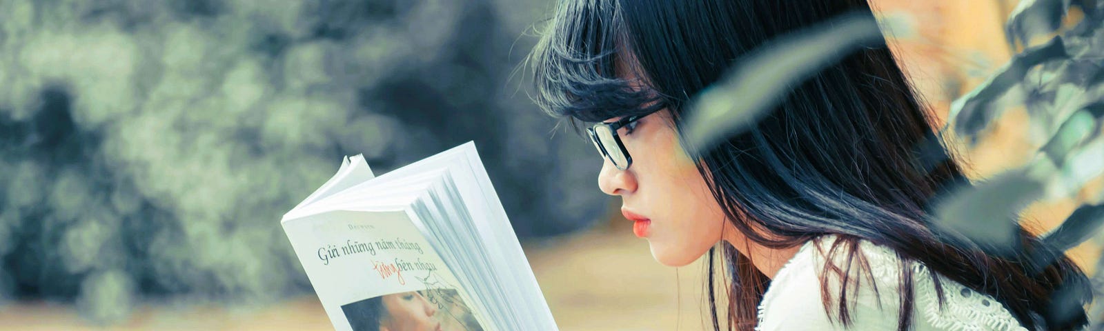 Asian woman reading a book outdoors.