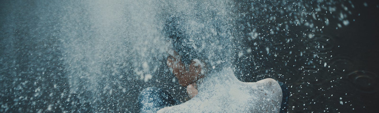 image of a person’s naked back and side of face. background dark blue with water droplets and a light shining on the person.
