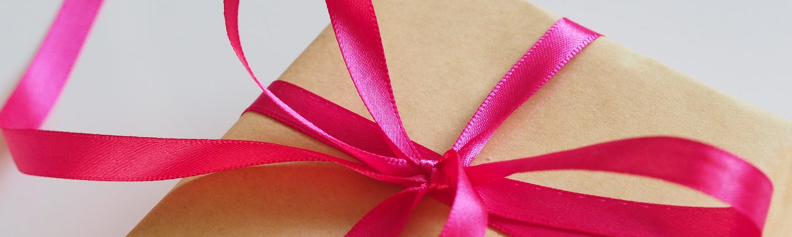 An image of a gift box wrapped in brown paper with a fushia ribbon tied into a bow on the top.
