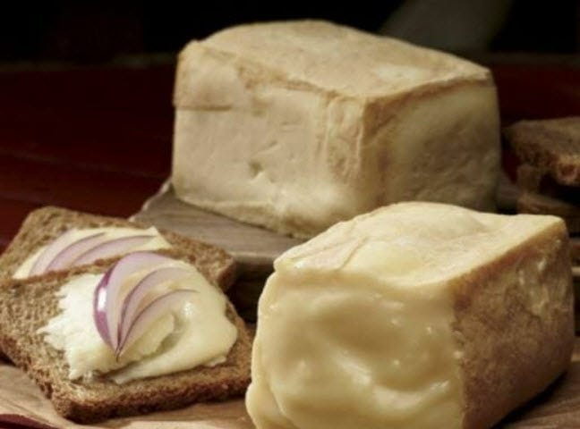 Two blocks of Limburger cheese next to two rye bread slices topped with Limburger and red onion slivers.