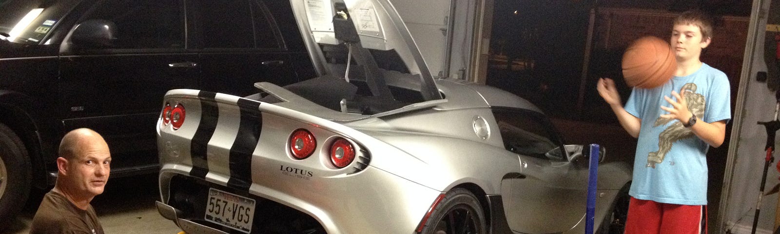 A man working on a sports car in his garage, with his son nearby.