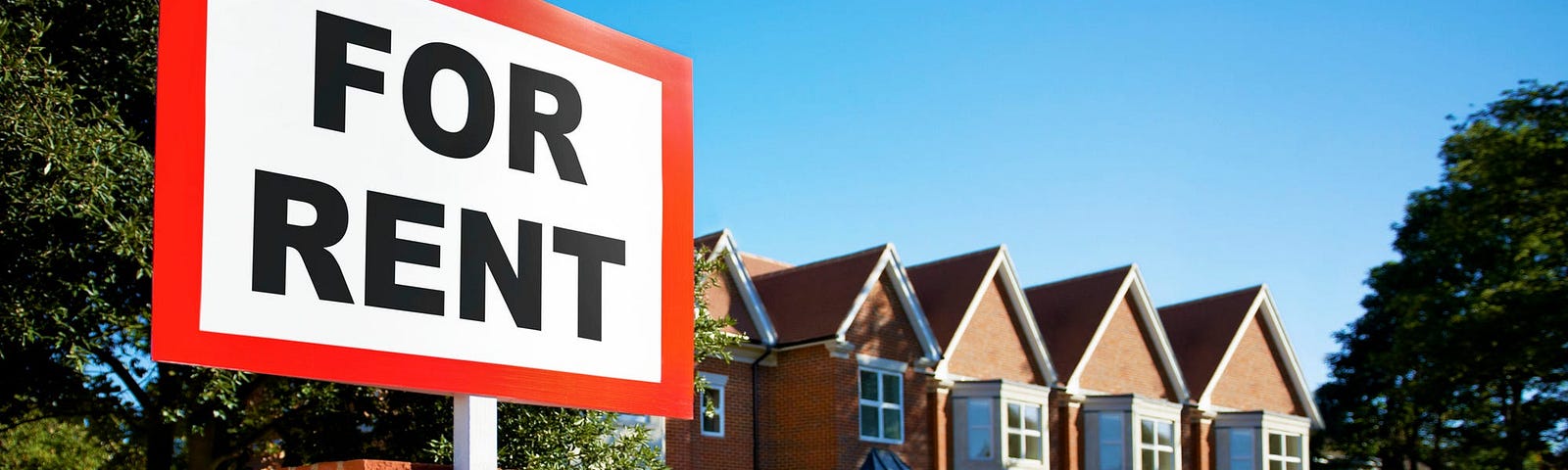 A “For Rent” sign in front of a row of homes.