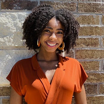 Jasmine Moore is pictured wearing an orange blouse against a limestone-and-brick background