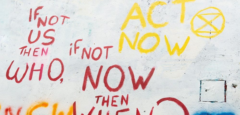 Colourful graffiti on a white wall that says: “act now”, “if not us then who”, and “if not now then when”.