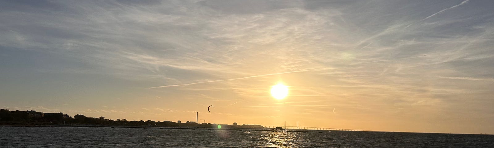 Hazy sky with the sun over Oresund bridge in Malmö, Sweden. Open water and waves. A person is windsurfing.