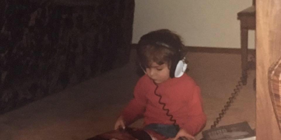 A child is listening to music through headphones while looking at a book in the 1970's