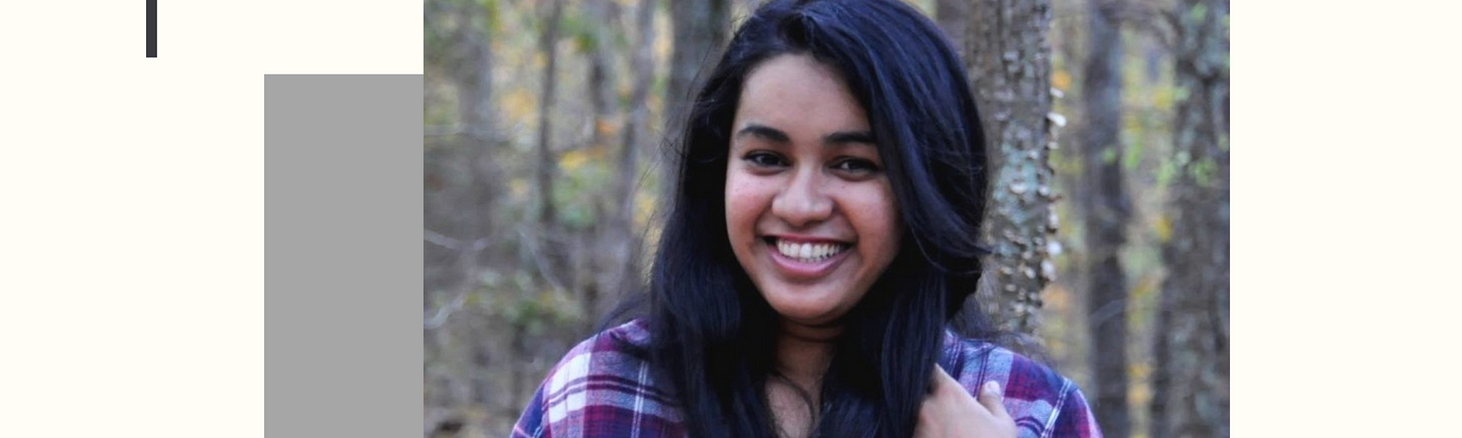 Nandita Gupta wearing a plaid purple shirt, smiling at the camera, with trees behind her.