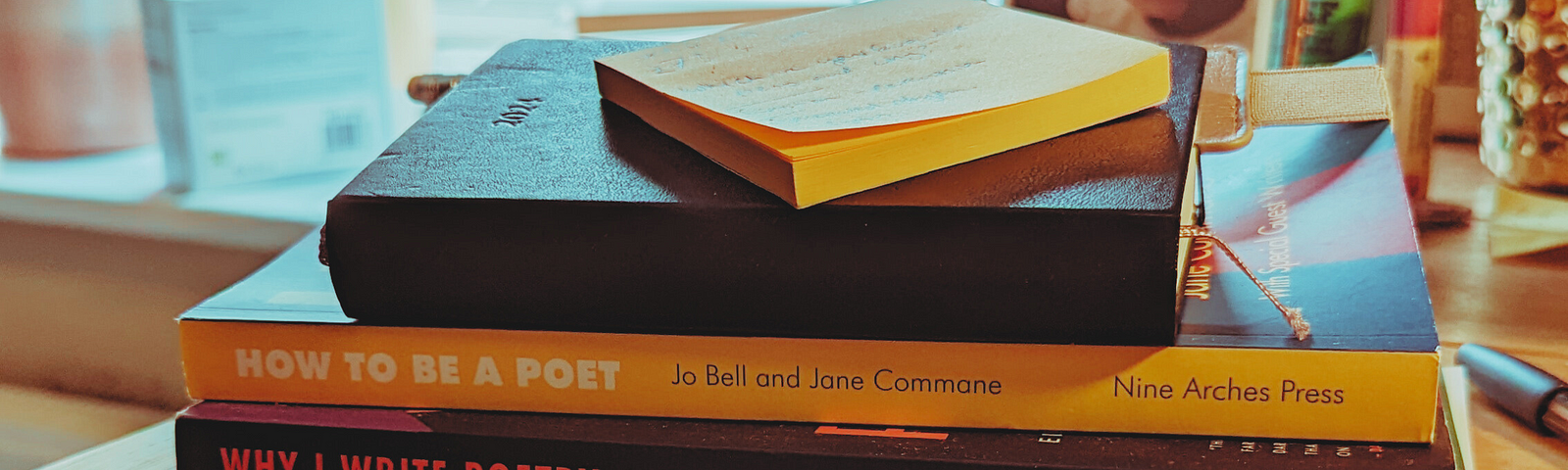 A stack of books on a desk. From bottom to top: The Poetry Review; Why I Write Poetr; How to be a Poet; 2024 diary; Post-its.