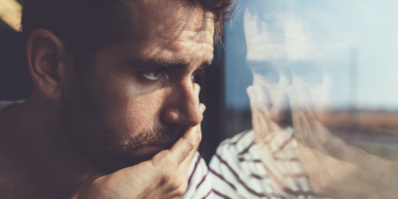 Sad man looking out of a window — How To Make Him Miss You Badly