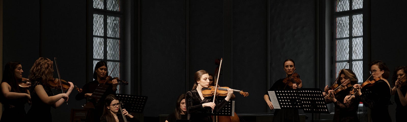 A violin soloist plays in front of an orchestra. She has a spotlight on her.