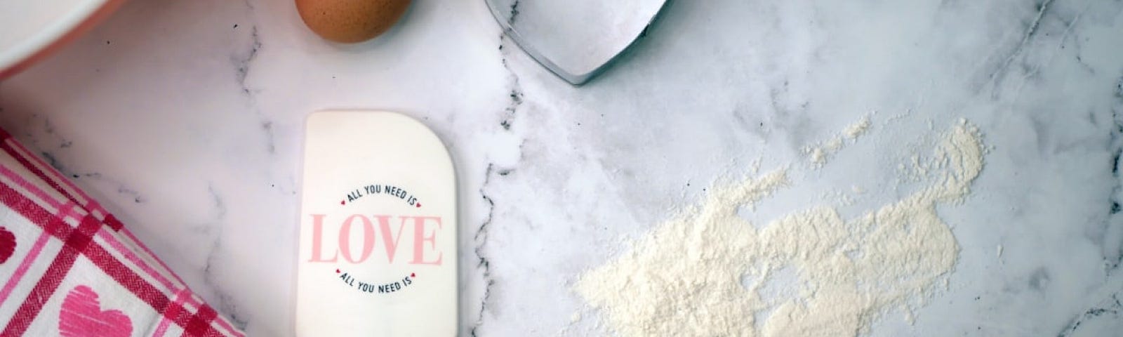 kitchen countertop with a bit of flour, eggs, and heart shaped cookie cutter