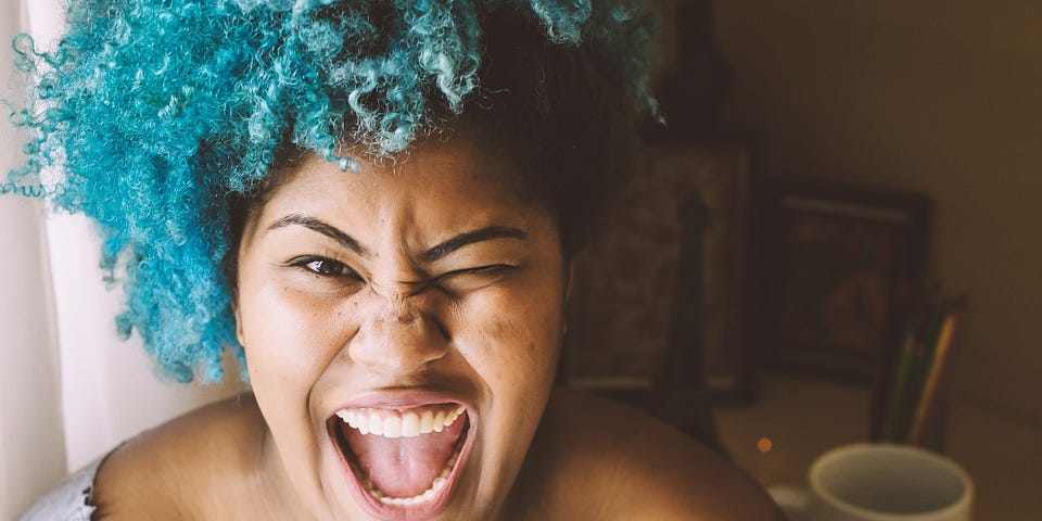 A photo of an excited, beautiful woman of color with blue hair.