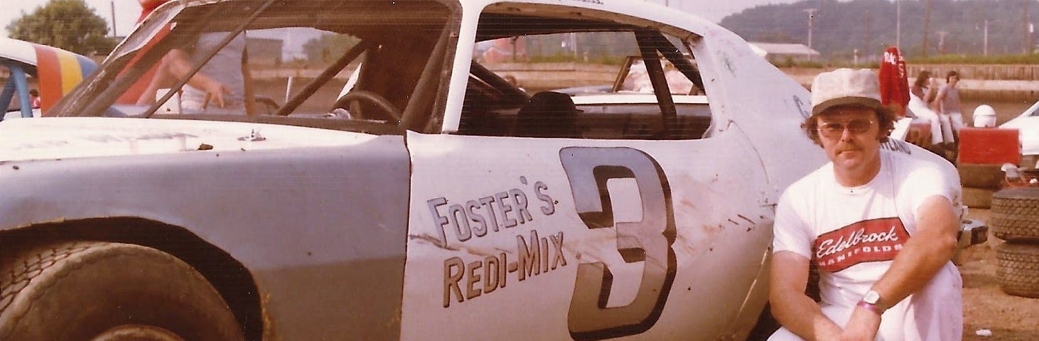 This photo shows a man squatting next to a white stock car.