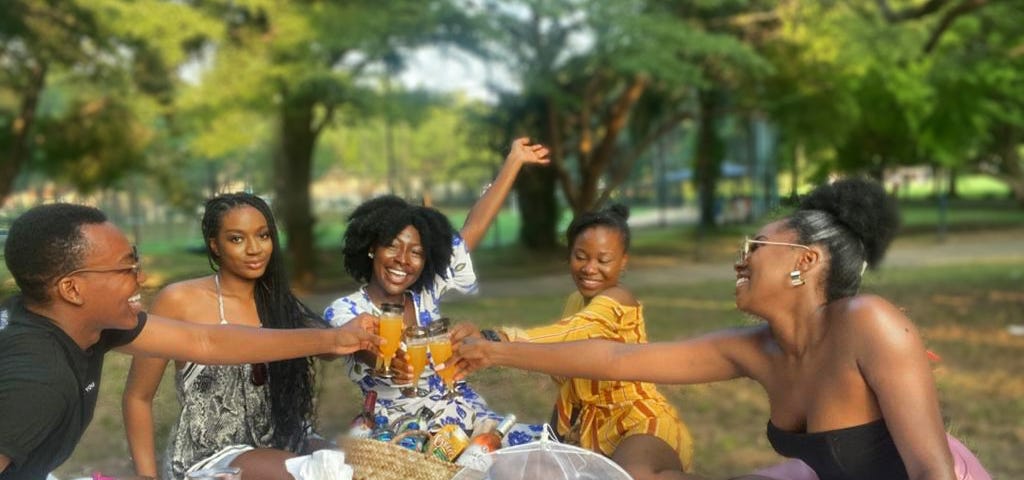 5 friends seated around a picnic, taking a toast with mimosas and smiles