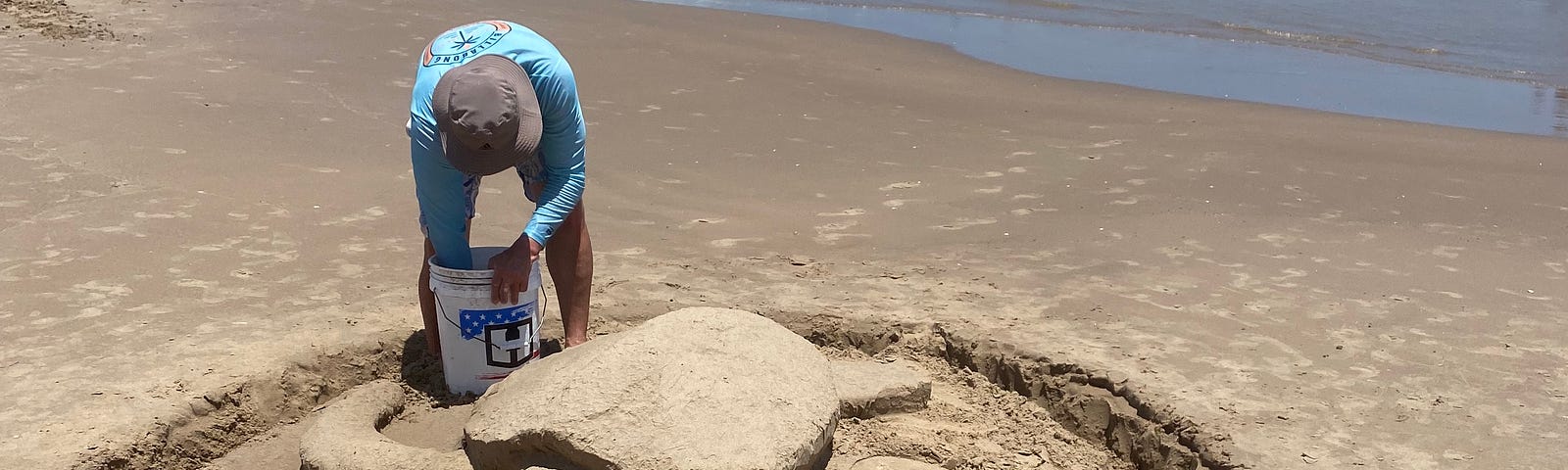 A man sculpting a sea turtle out of sand.