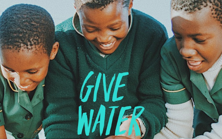 “Give Water Give Life” — 3 people washing their hands, excitedly, from a clean water drinking well.