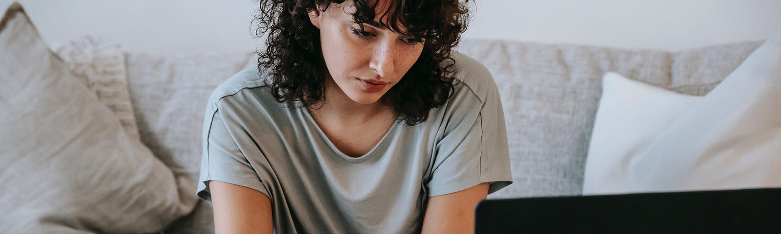 Gorgeous woman with lush black hair writing in a journal staring at a laptop screen