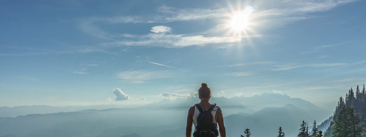 person standing on a mountain watching the valley with the sun in the background