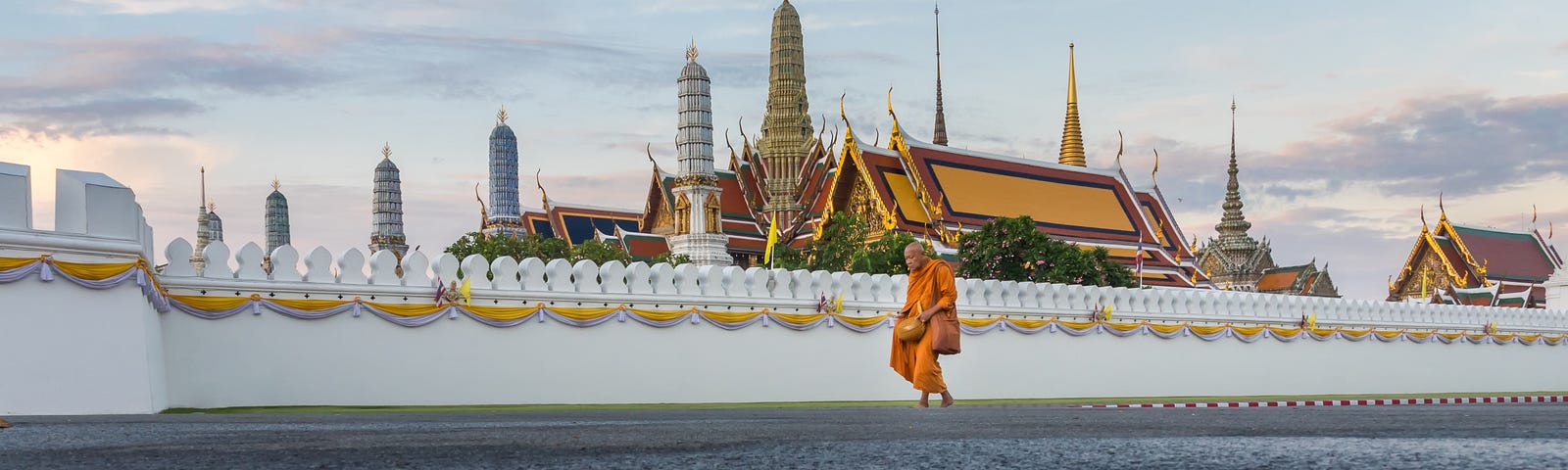 A photograph of a monk walking in the morning after the rain in front of the Temple of the Emerald Buddha (Wat Phra Kaew), part of the Grand Palace, in Bangkok, Thailand