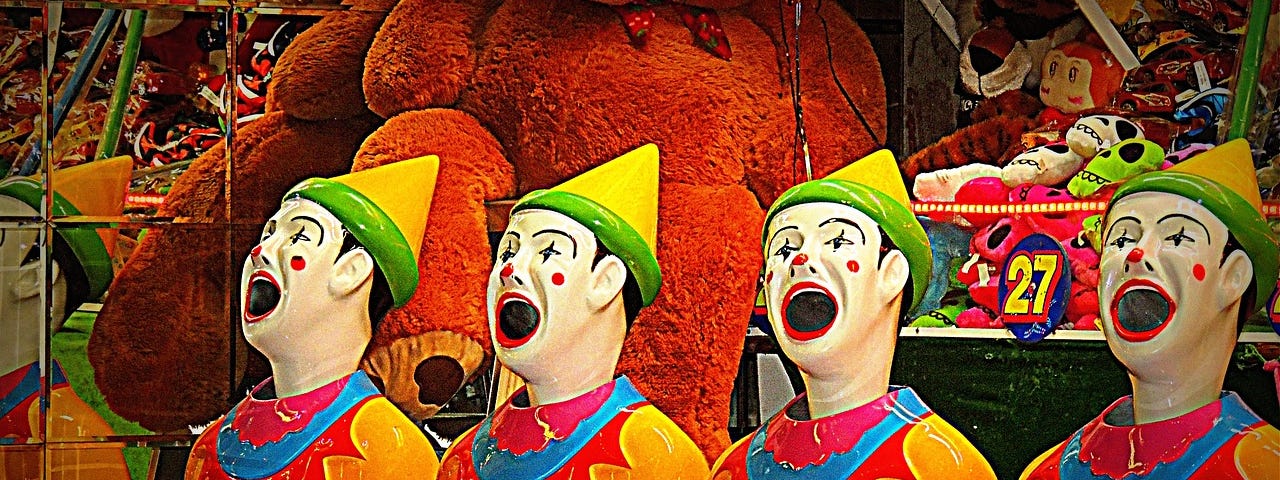 Four fake clowns have their mouths open as part of a game of chance at a carnival