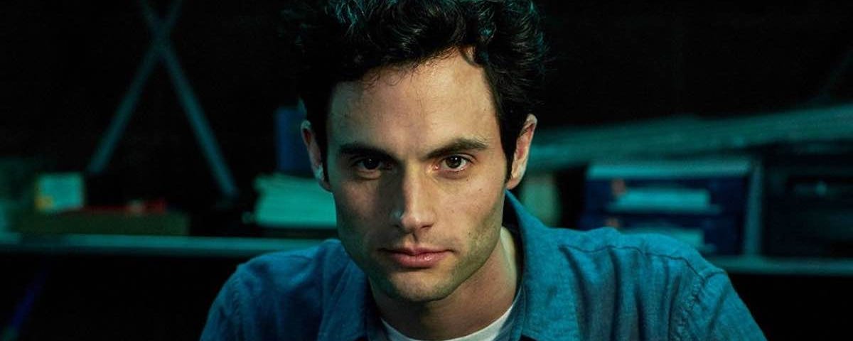 Joe Goldberg, played by Penn Badgley, stares intensely into the camera against a darkened background.