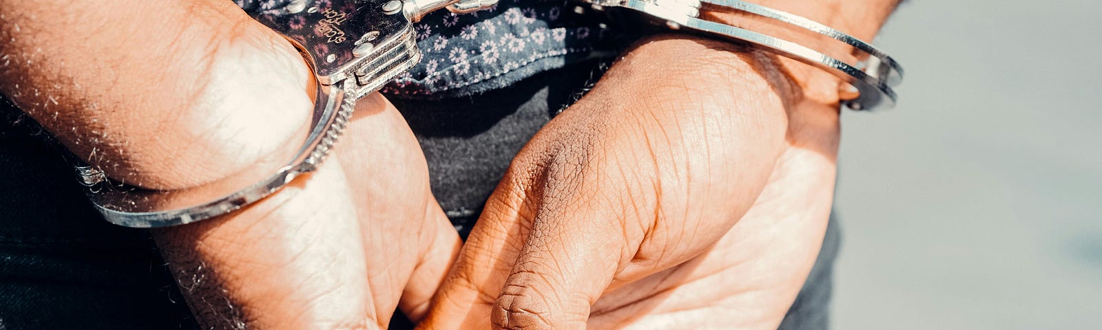 Picture of a man with his hands behind his back, wearing handcuffs.