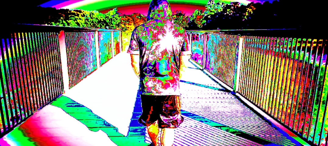 A picture of a man with a hoodie on walking on a bridge that leads to a rainbow portal. The entire image is vividly colored in a psychedelic-type way.