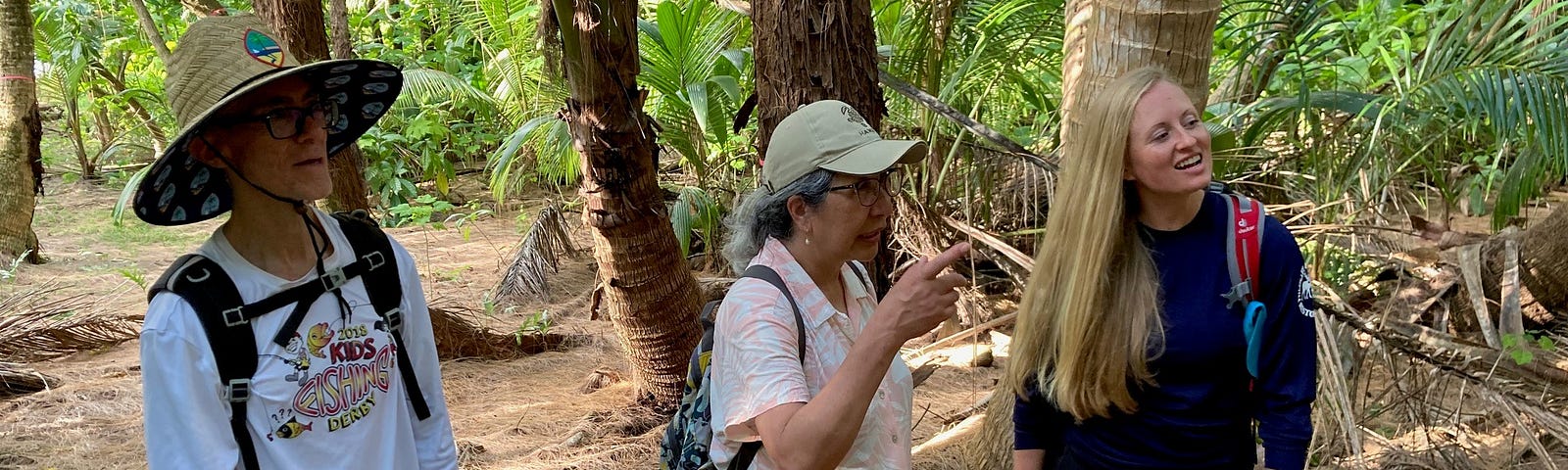 Ruth Utzurrum (center) on Island Dano, Guam, standing with Jay Gutierrez (left), Chief of Guam’s Division of Aquatic and Wildlife Resources (DAWR), and Lauren Thompson (right), wildlife biologist for DAWR. They are standing in a jungle with palm trees in the backdrop.