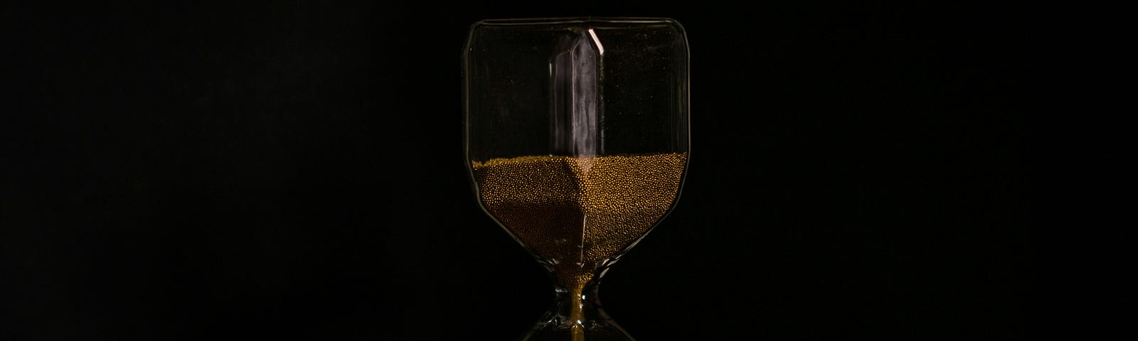 An hourglass on a bed of red rose petals, set in a black background.