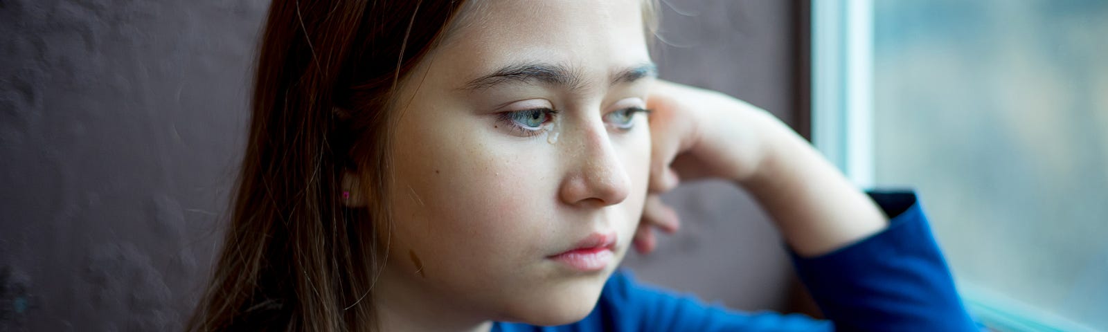 Little girl sad and alone staring out of window