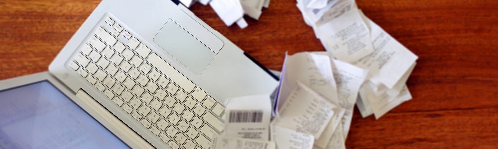 An open laptop surrounded by piles of receipts.