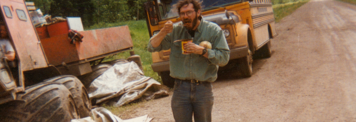 A man eating from a can with a school bus in the background.