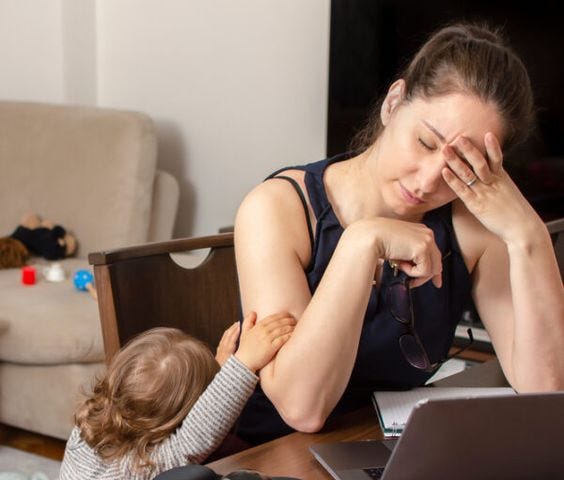 A woman trying to work on her laptop with her toddler pulling on her arm.