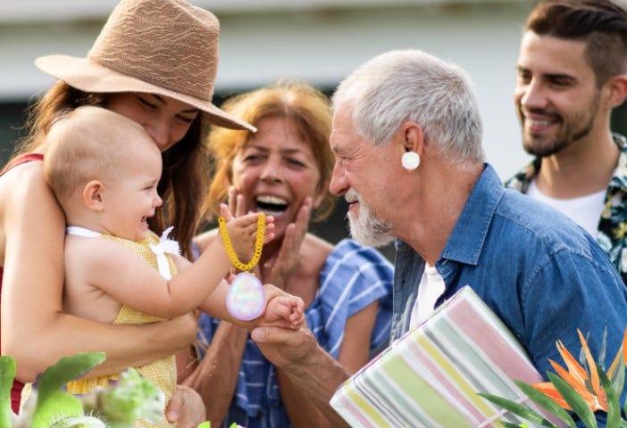 Multiple generations of a family with opal gems in view and plants behind a hedge.