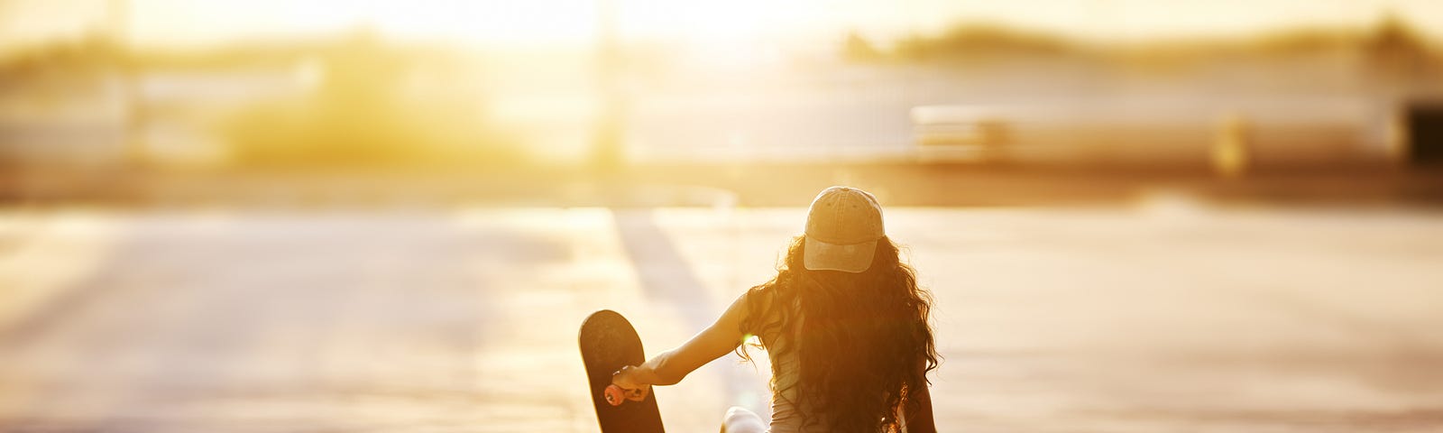 A girl sitting with her skateboard, watching the sunset.