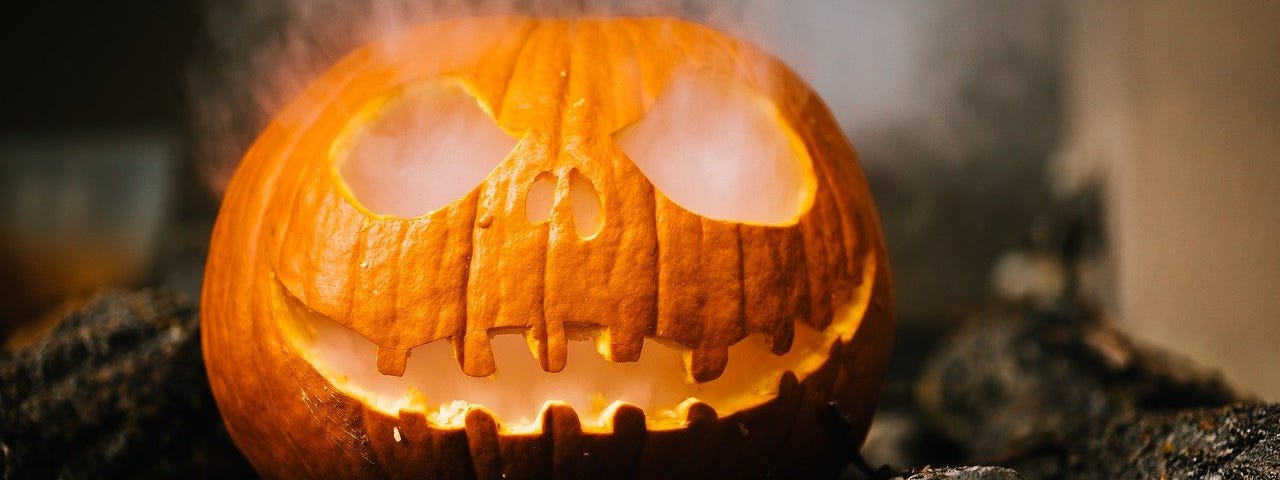 A smoking Halloween style carved pumpkin on a pile of woods.