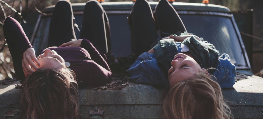 two teenage girls lying on the hood of a car