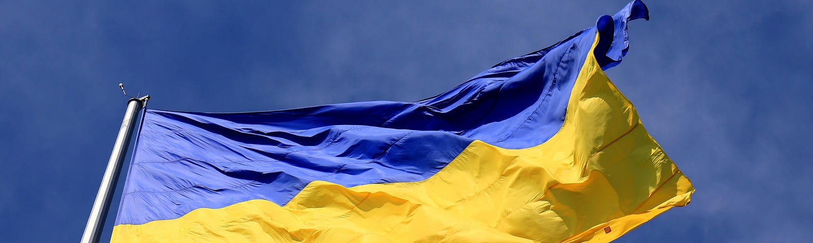 A photo of the bright blue and yellow Ukrainian flag flying agianst a blue sky.
