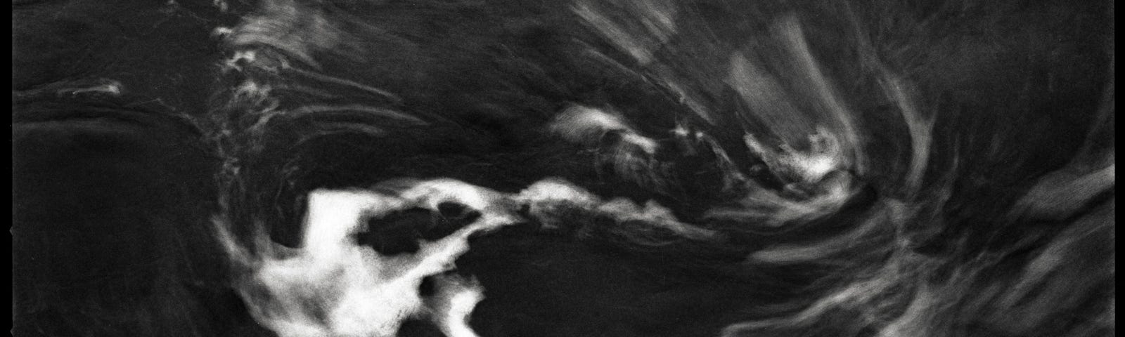 A black and white film photograph showing white swirling sea foam against a dark gray ocean.